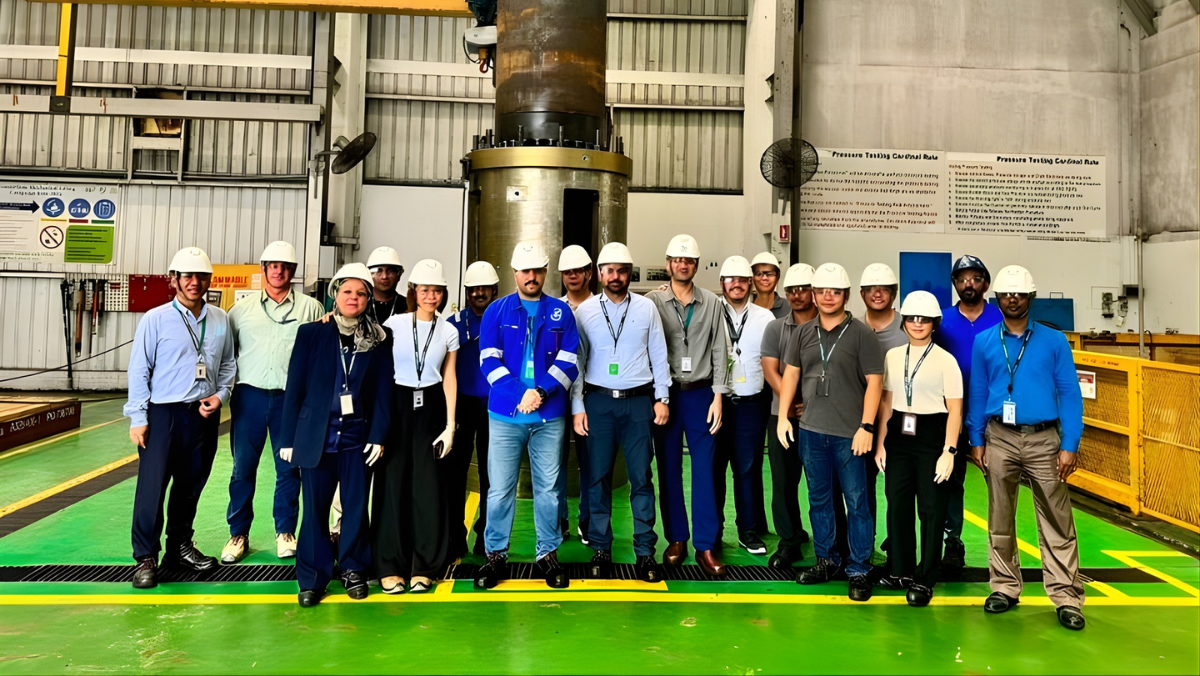 Engineers wearing hard hats pose inside an industrial oilfield facility during a site visit