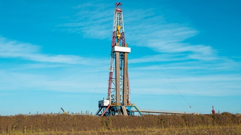 Onshore oil drilling rig standing in dry field under blue sky